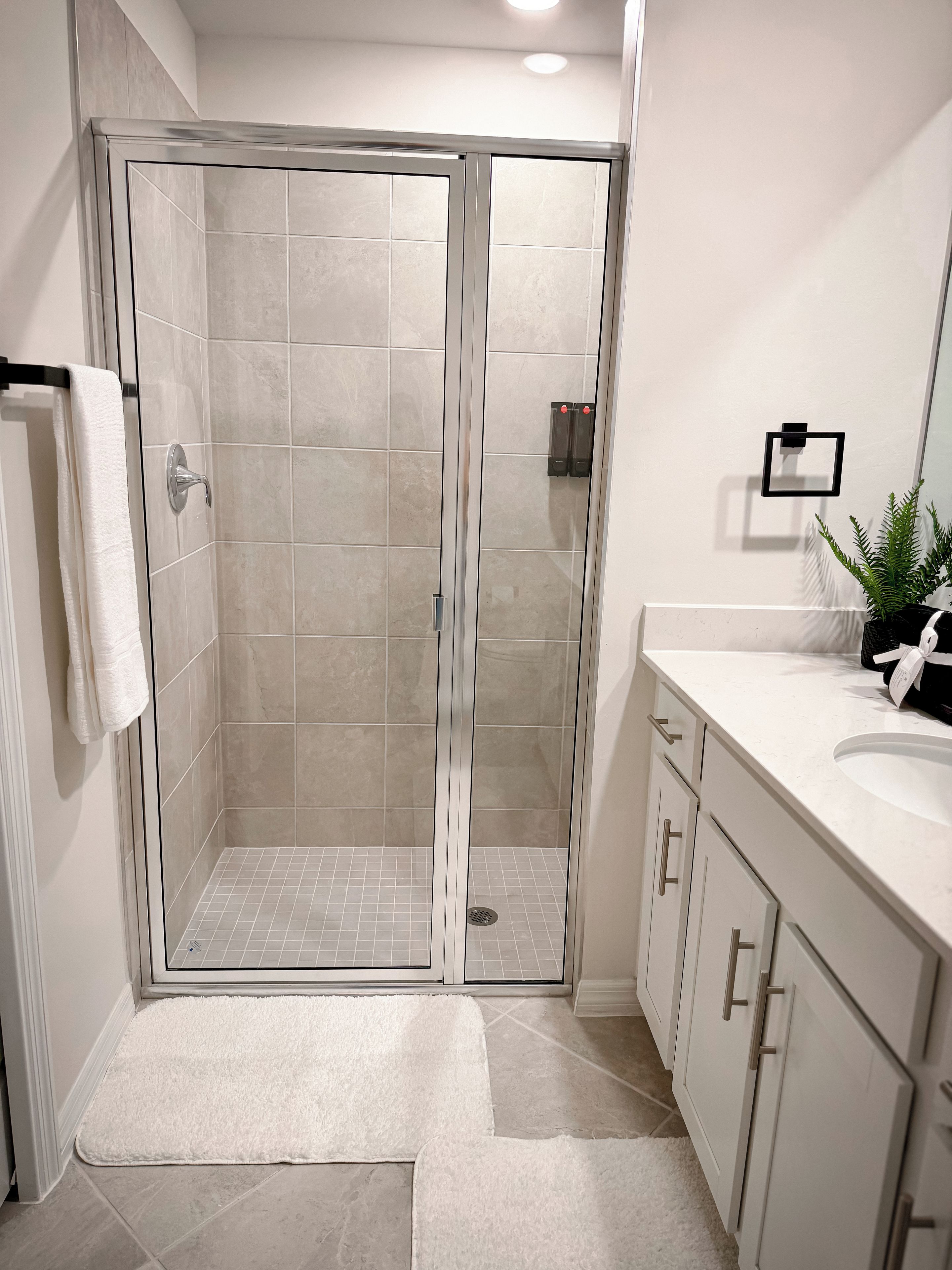 A modern bathroom with a glass-enclosed shower, white tiled walls, and a white vanity with a sink.