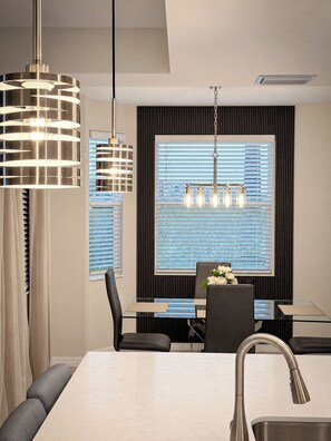 A modern dining area with a glass table, black chairs, and a pendant light fixture.