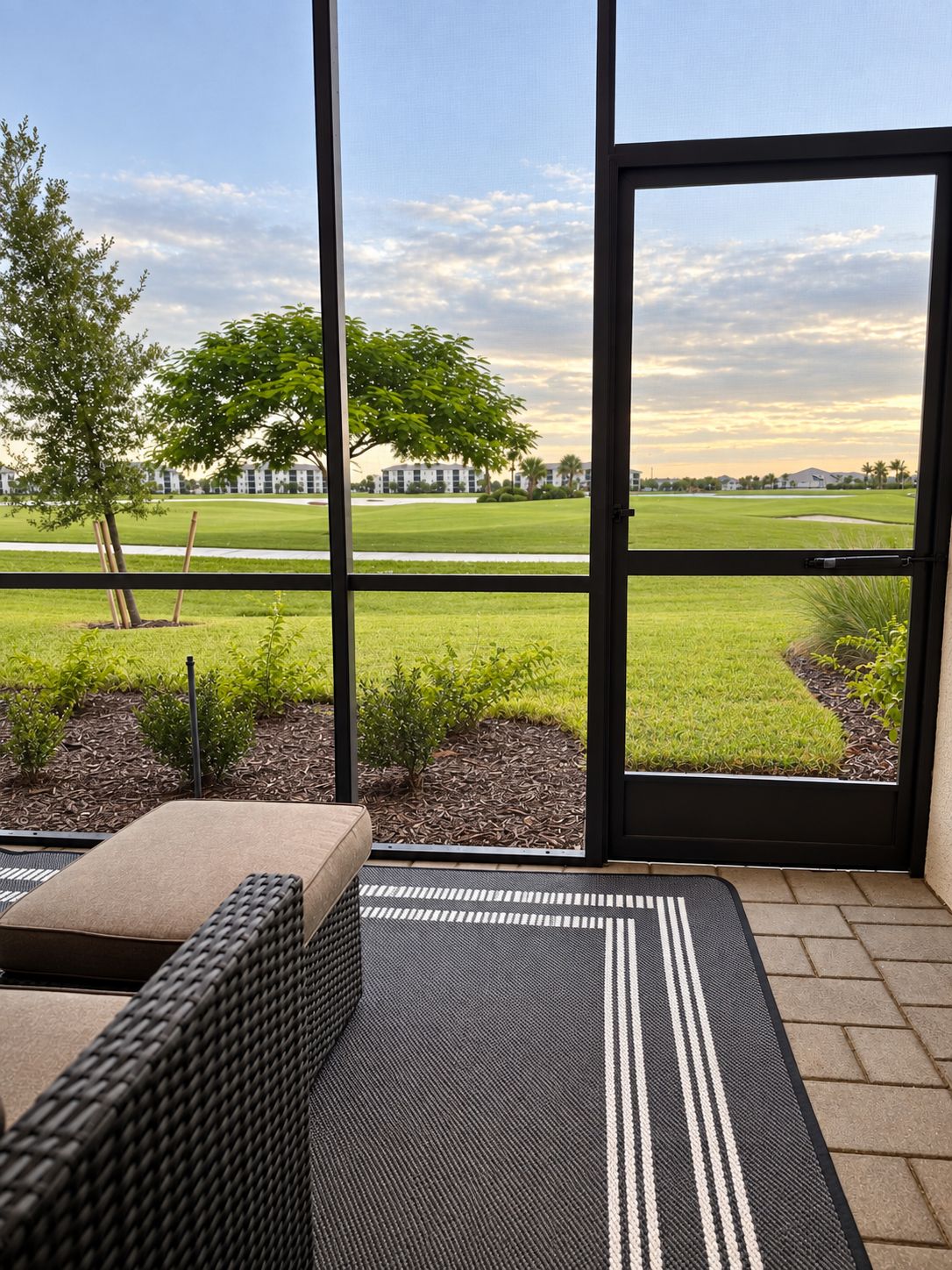 A room with a view of a golf course, a wicker sofa, and a black and white striped rug.