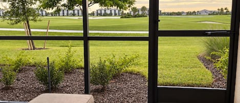 A room with a view of a golf course, a wicker sofa, and a black and white striped rug.