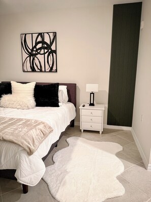 A bedroom with a bed, a nightstand, a lamp, a large abstract painting, and a green vertical panel.