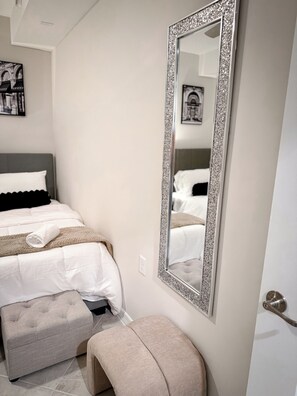 A bedroom with a bed, a large mirror, a bench, and a door.