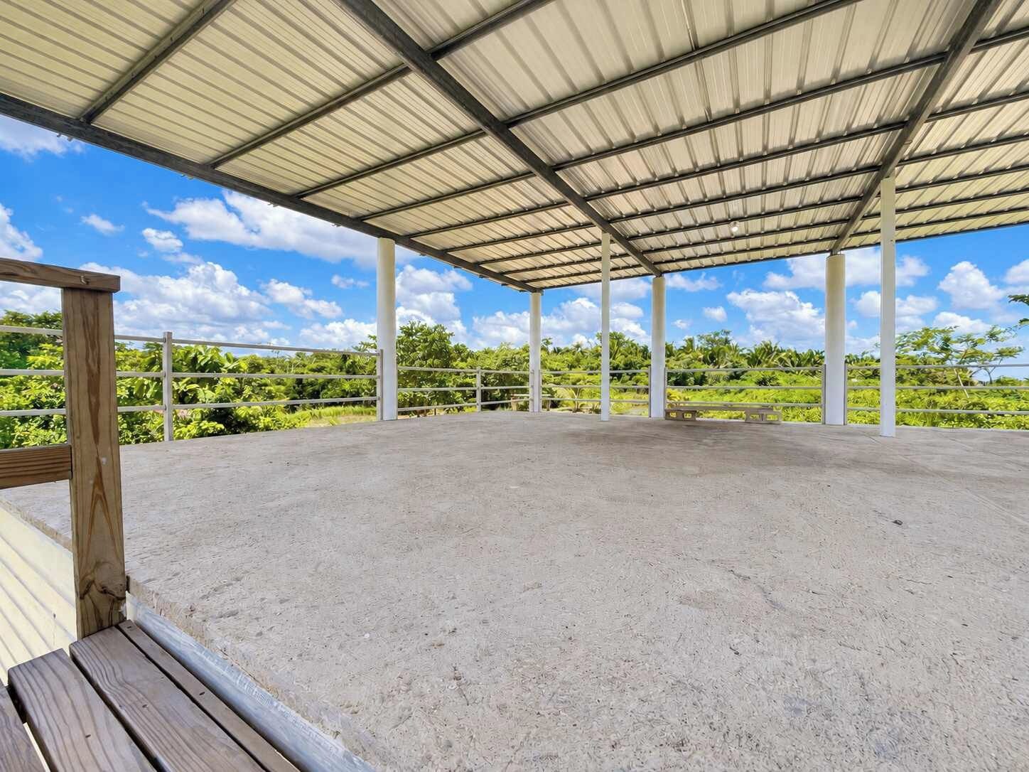 An open-air pavilion with a concrete floor and metal roof, surrounded by greenery.