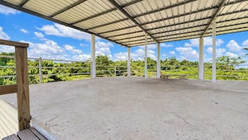 An open-air pavilion with a concrete floor and metal roof, surrounded by greenery.
