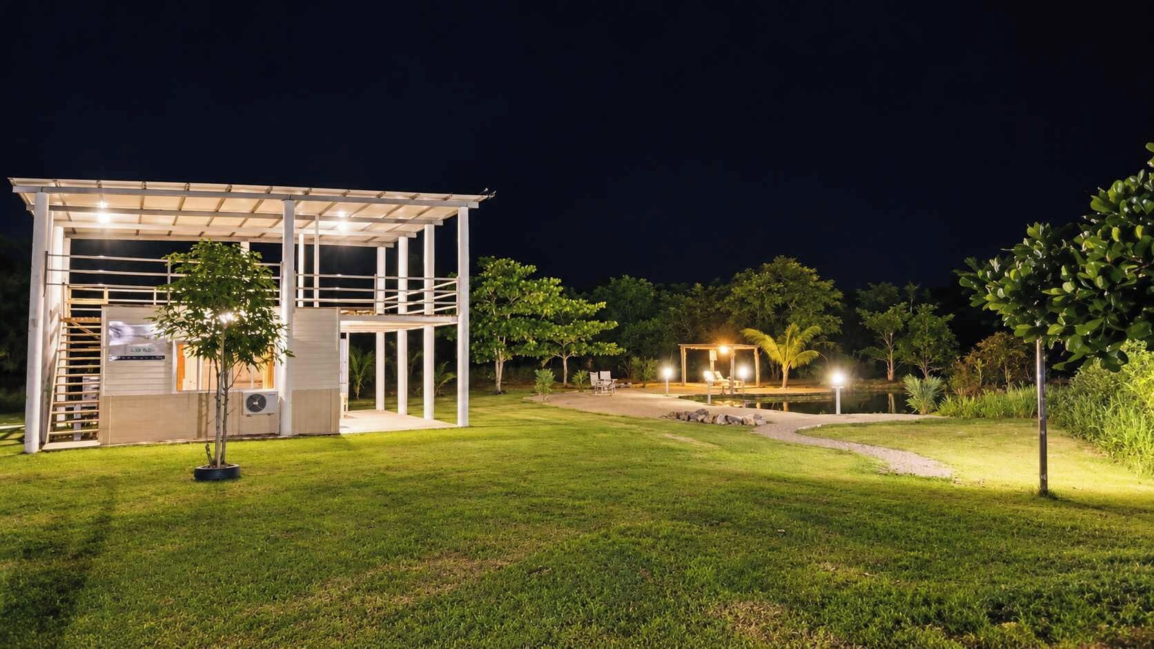 A modern outdoor structure with a covered seating area and a small pool, surrounded by well-maintained grass and trees.