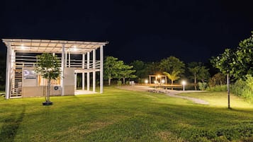 A modern outdoor structure with a covered seating area and a small pool, surrounded by well-maintained grass and trees.