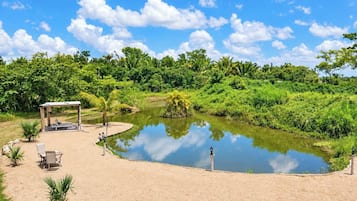 A serene outdoor area with a pond, a wooden gazebo, and a sandy seating area.
