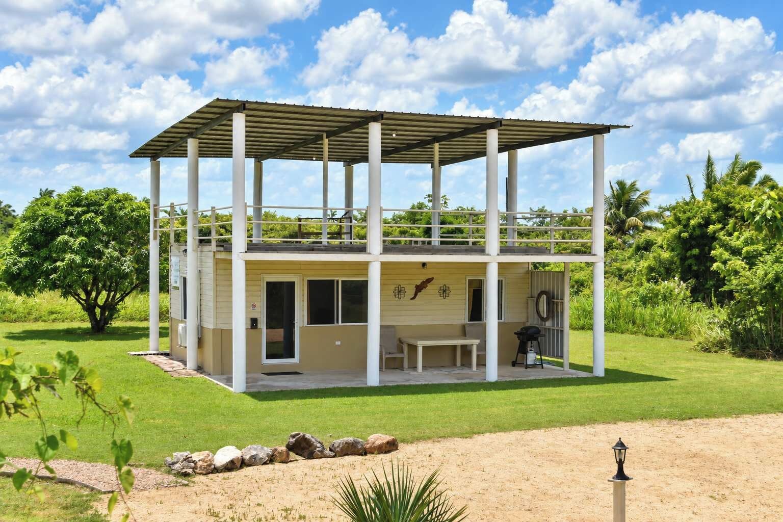 Un edificio de dos plantas con un porche cubierto, zona de barbacoa y vistas al follaje circundante.