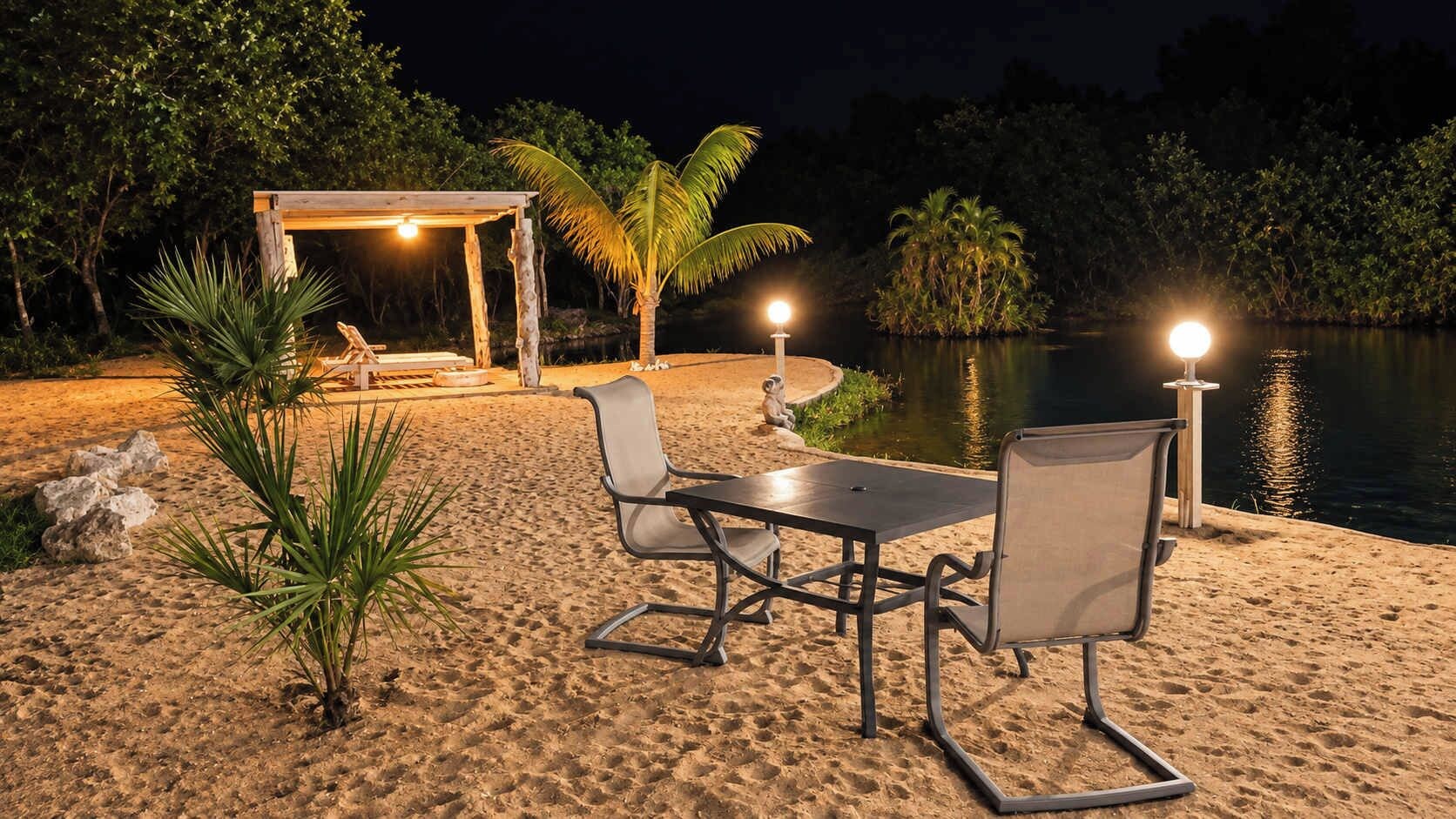 A beachside setting with a table and chairs, a covered seating area, and a body of water.