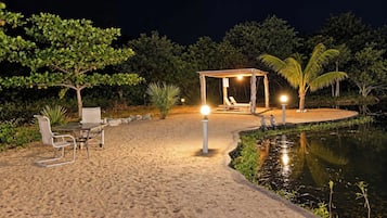 A beachside area with a table and chairs, a covered seating area, and a small pond.