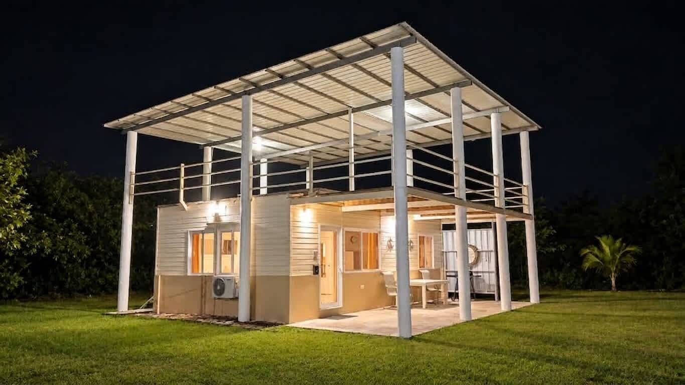 Een gelijkvloers huis met een overdekt terras, een zichtbare airconditioning en een goed verlicht interieur.