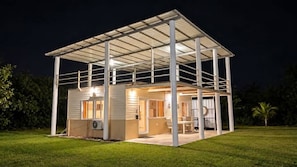 Una casa de un piso con un patio cubierto, un equipo de aire acondicionado visible y un interior bien iluminado.