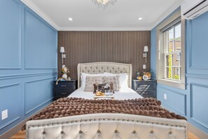 A bedroom with a tufted headboard, a large fluffy rug, and a window with a view of buildings. - Charming 2BR Near Back Bay (Boston)