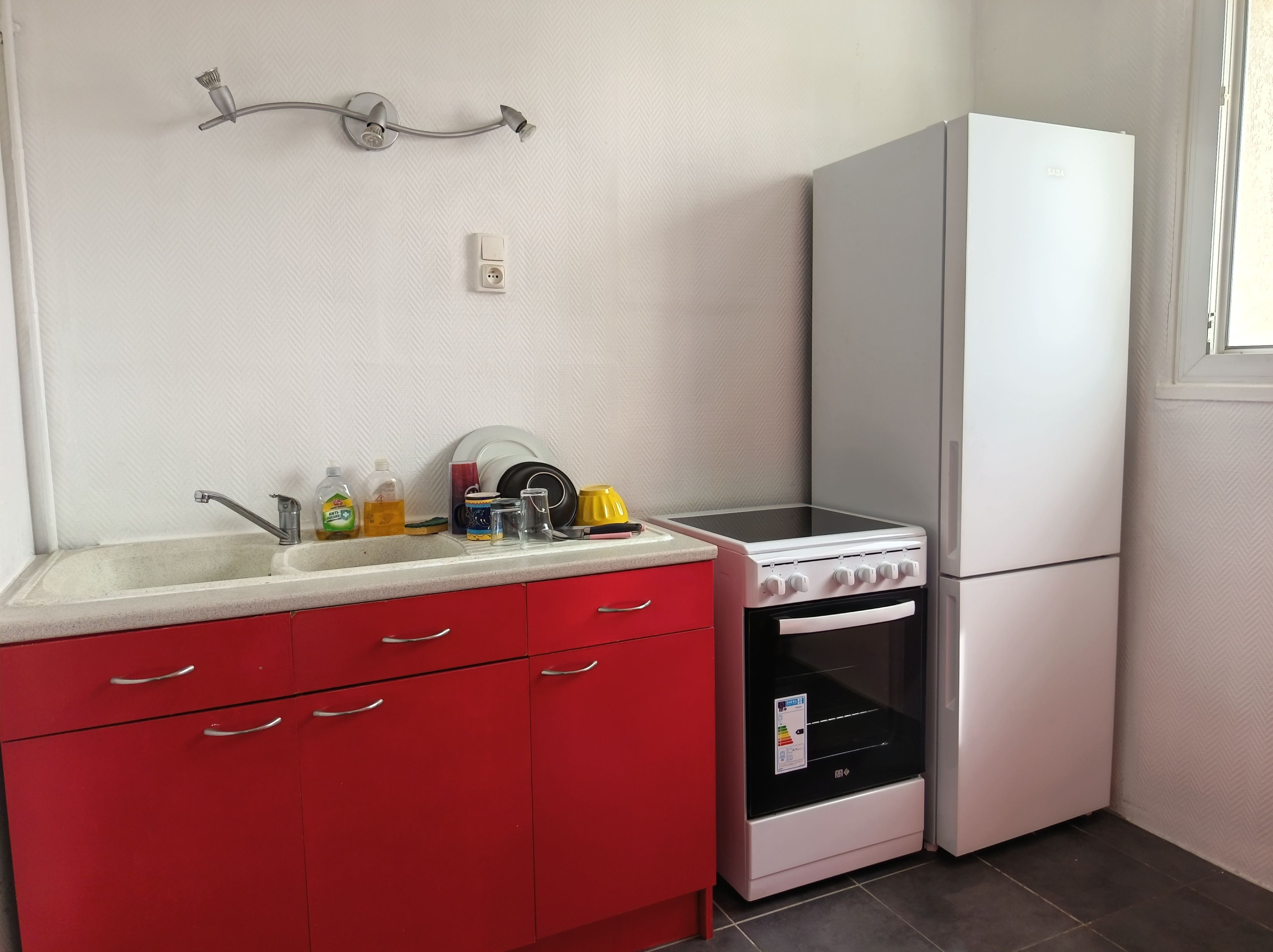 A kitchen with a sink, red cabinets, a stove, and a white refrigerator.