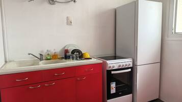 A kitchen with a sink, red cabinets, a stove, and a white refrigerator.