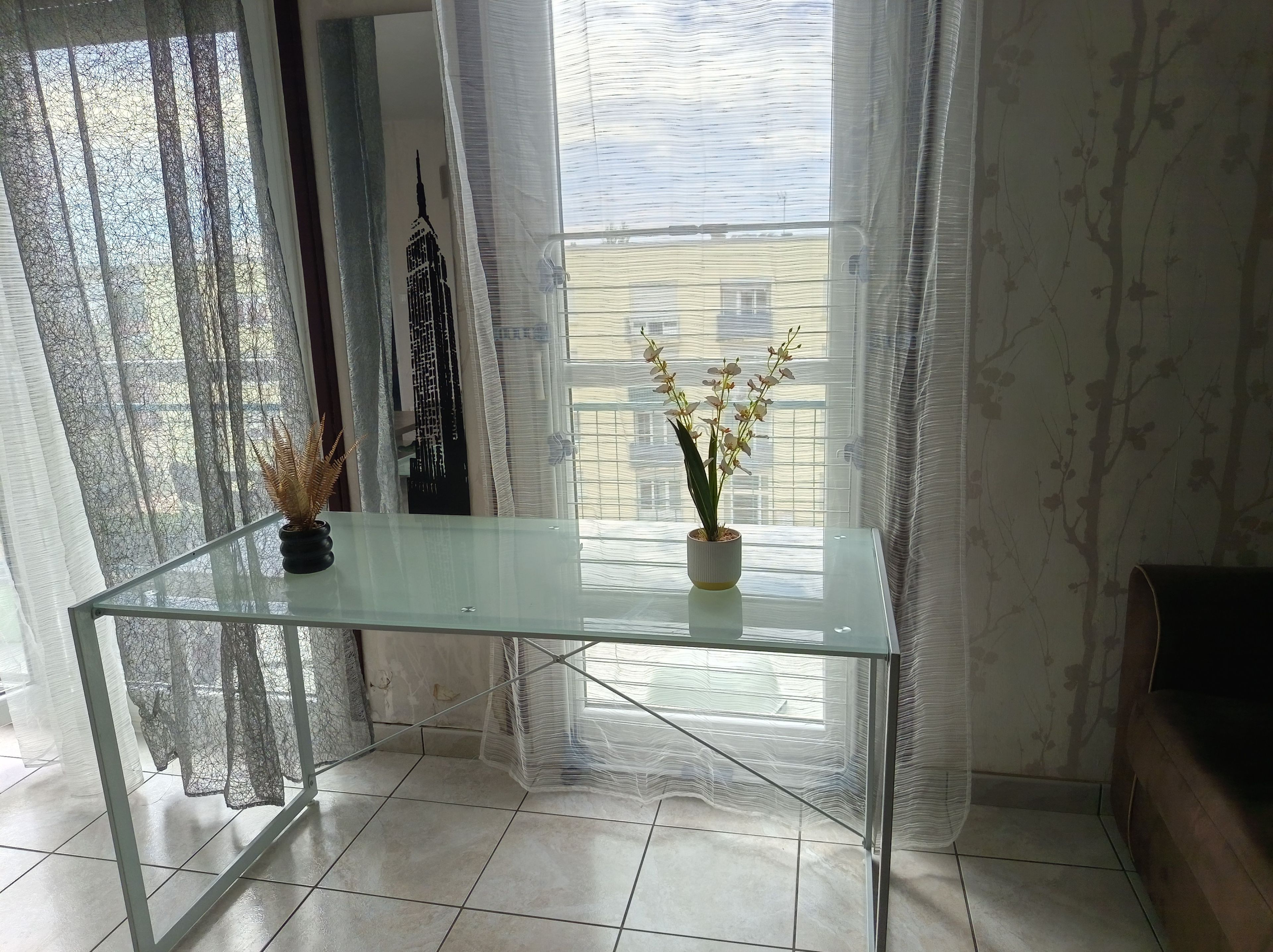 Una habitación con una mesa de vidrio, una planta en maceta y cortinas translúcidas.