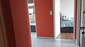 Un couloir aux murs rouges mène à une chambre à coucher qui contient un lit et une table de chevet.