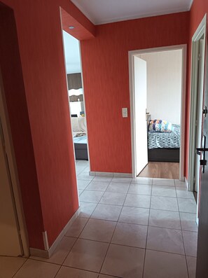 Un couloir aux murs rouges mène à une chambre à coucher qui contient un lit et une table de chevet.