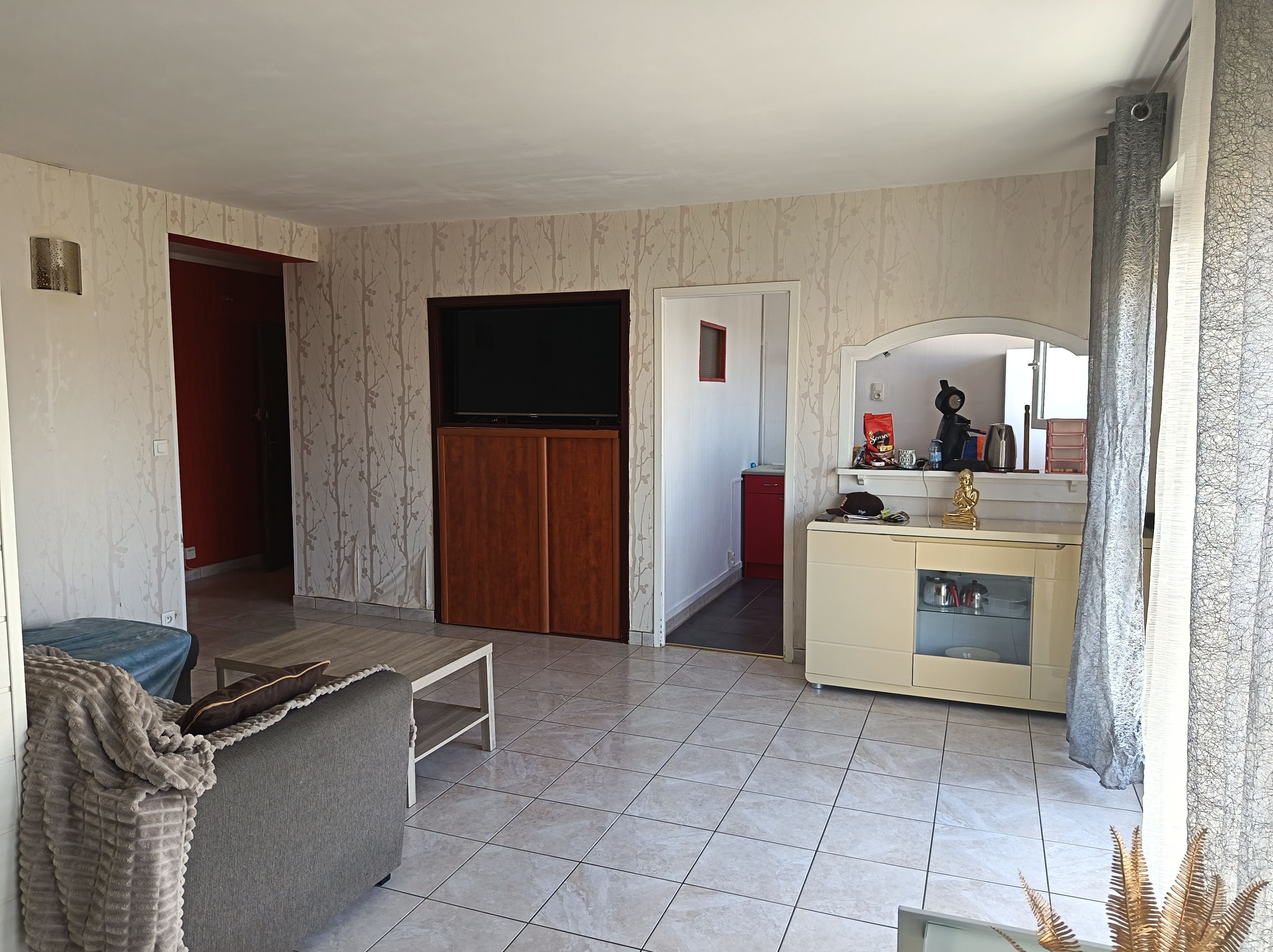 A living room with a sofa, a TV, a cabinet, and a red door.