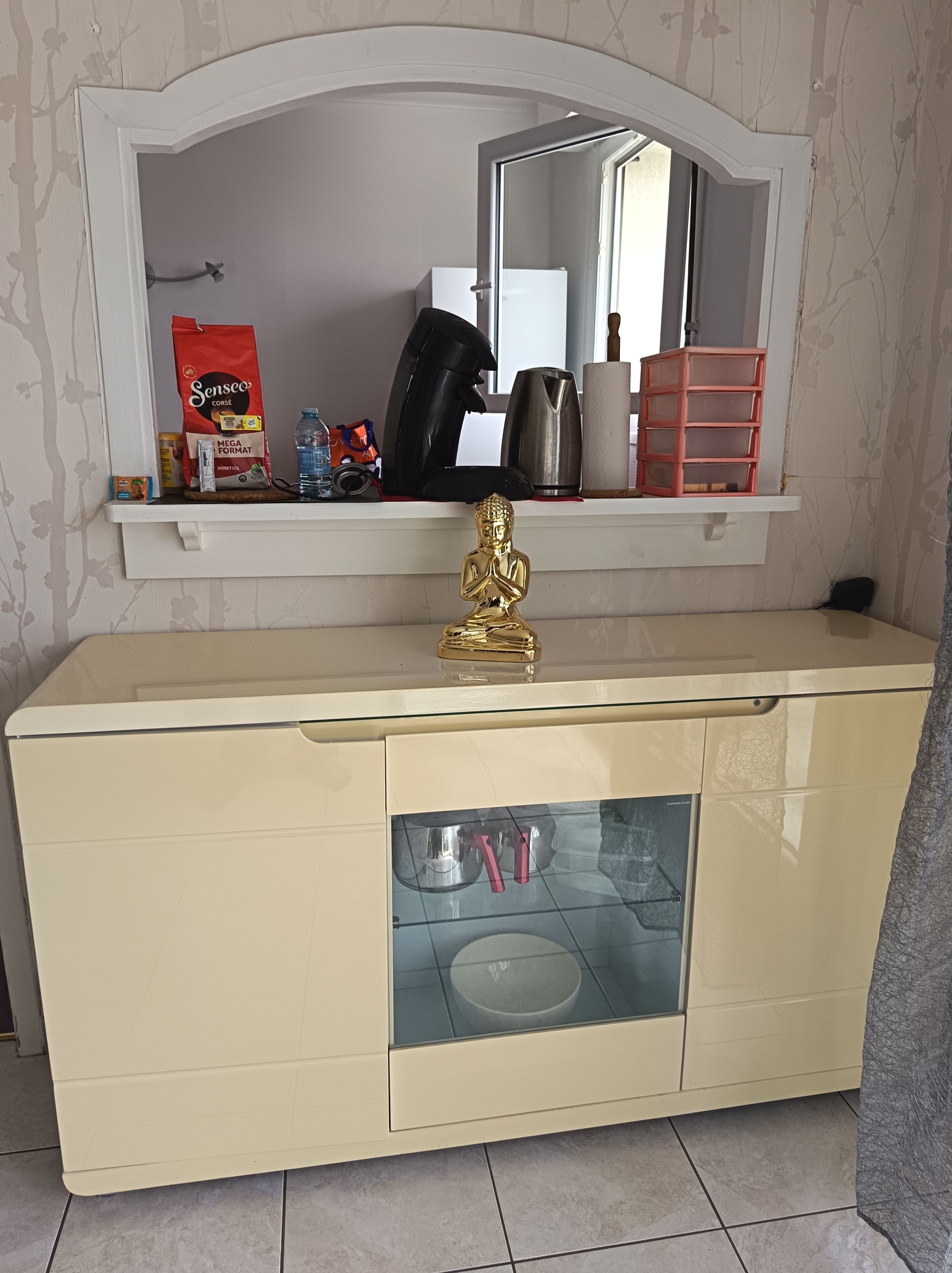 Un tocador de baño con un espejo, una estatua dorada de Buda y varios artículos de aseo.