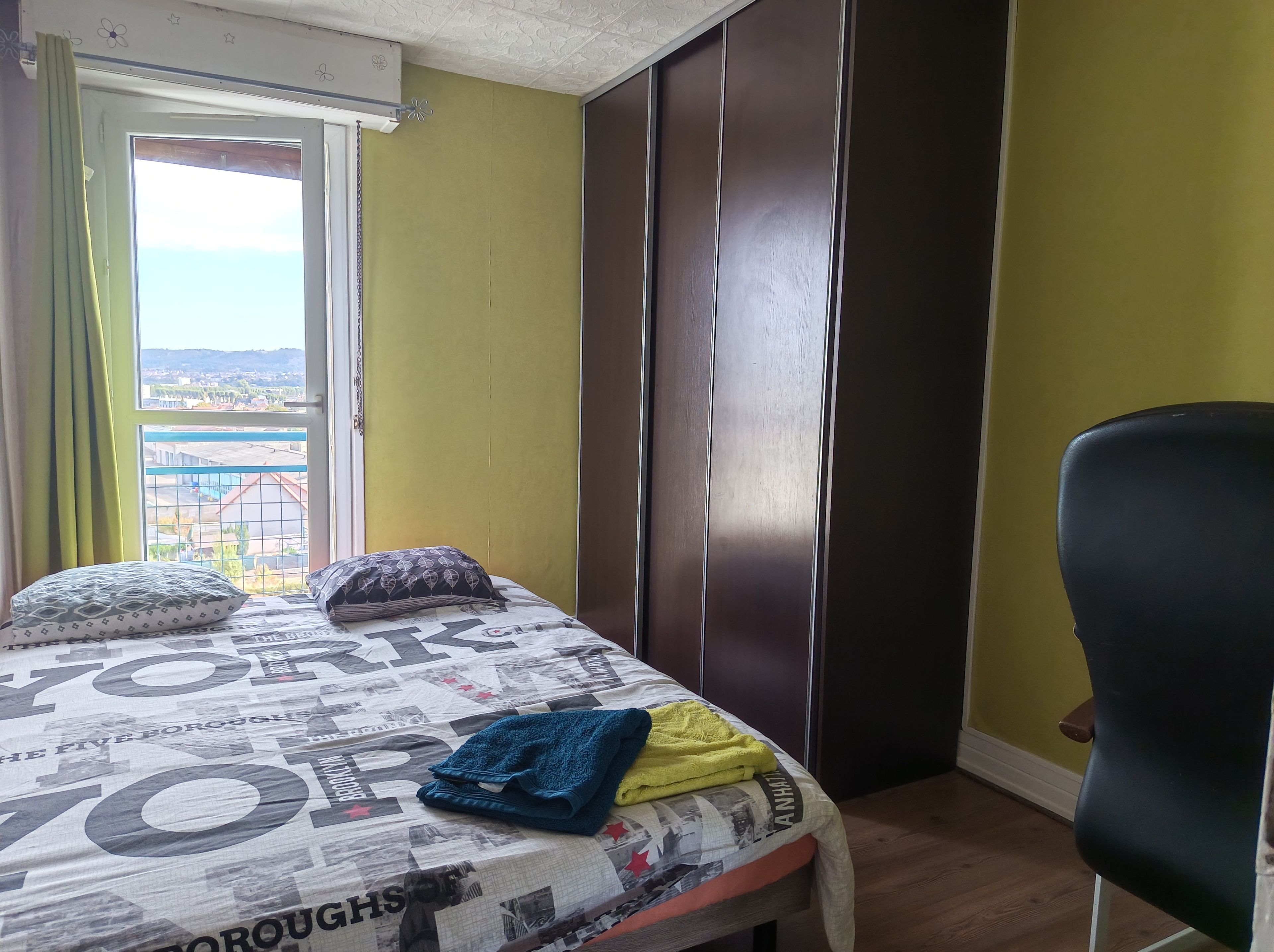 Un dormitorio con cama, una silla, armario y ventana con vistas.