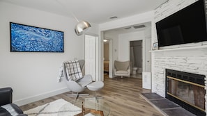 A modern living room with a fireplace, a mounted TV, and a large abstract painting. - Beautifully updated East Hampton retreat with a heated pool, sauna, and... (East Hampton)