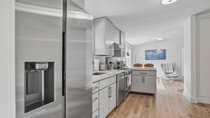A modern kitchen with stainless steel appliances, a built-in oven, and a microwave. There is a dining area with a chair and a table. - Beautifully updated East Hampton retreat with a heated pool, sauna, and... (East Hampton)
