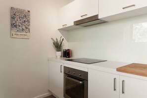 Eine moderne Küche mit weißen Schränken, einem Edelstahlbackofen, einer schwarzen Induktionskochplatte und einer Holz Arbeitsplatte.
