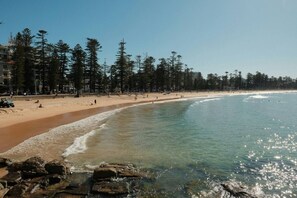 A beach with clear water, sandy shore, and trees. - Manly 2BR | 5 Min Walk to Beach + Parking (Manly)