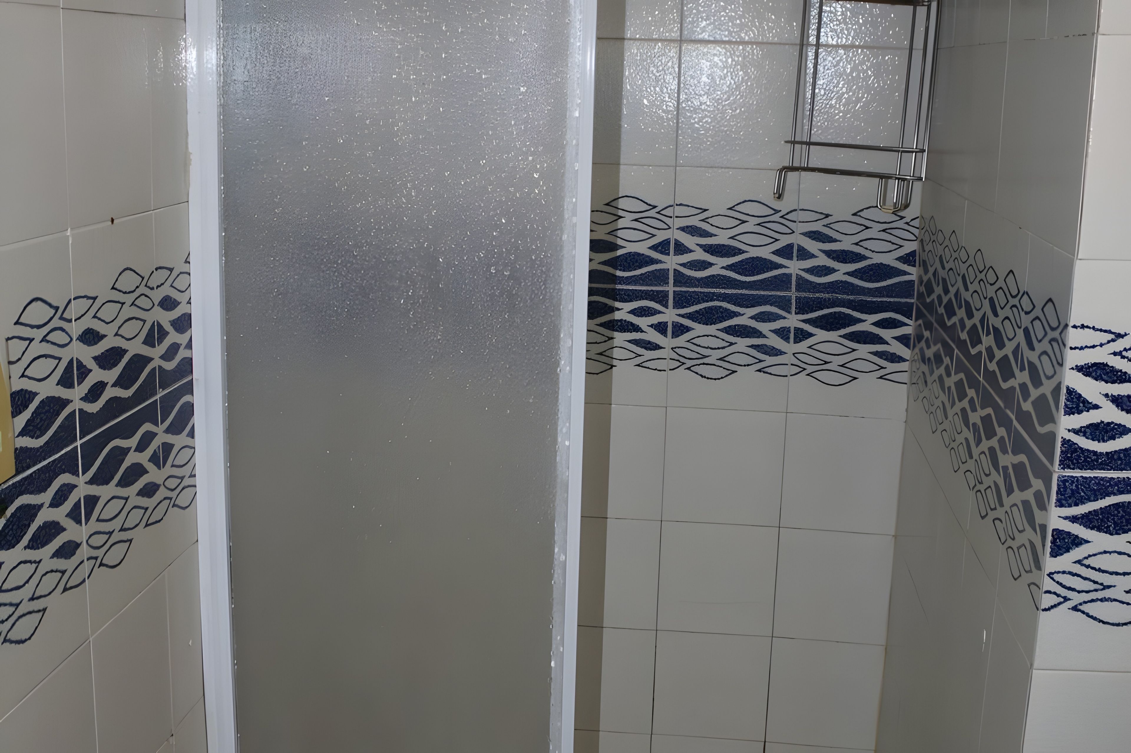 Uno spazio doccia con piastrelle e un motivo geometrico sulle pareti e un soffione in metallo.