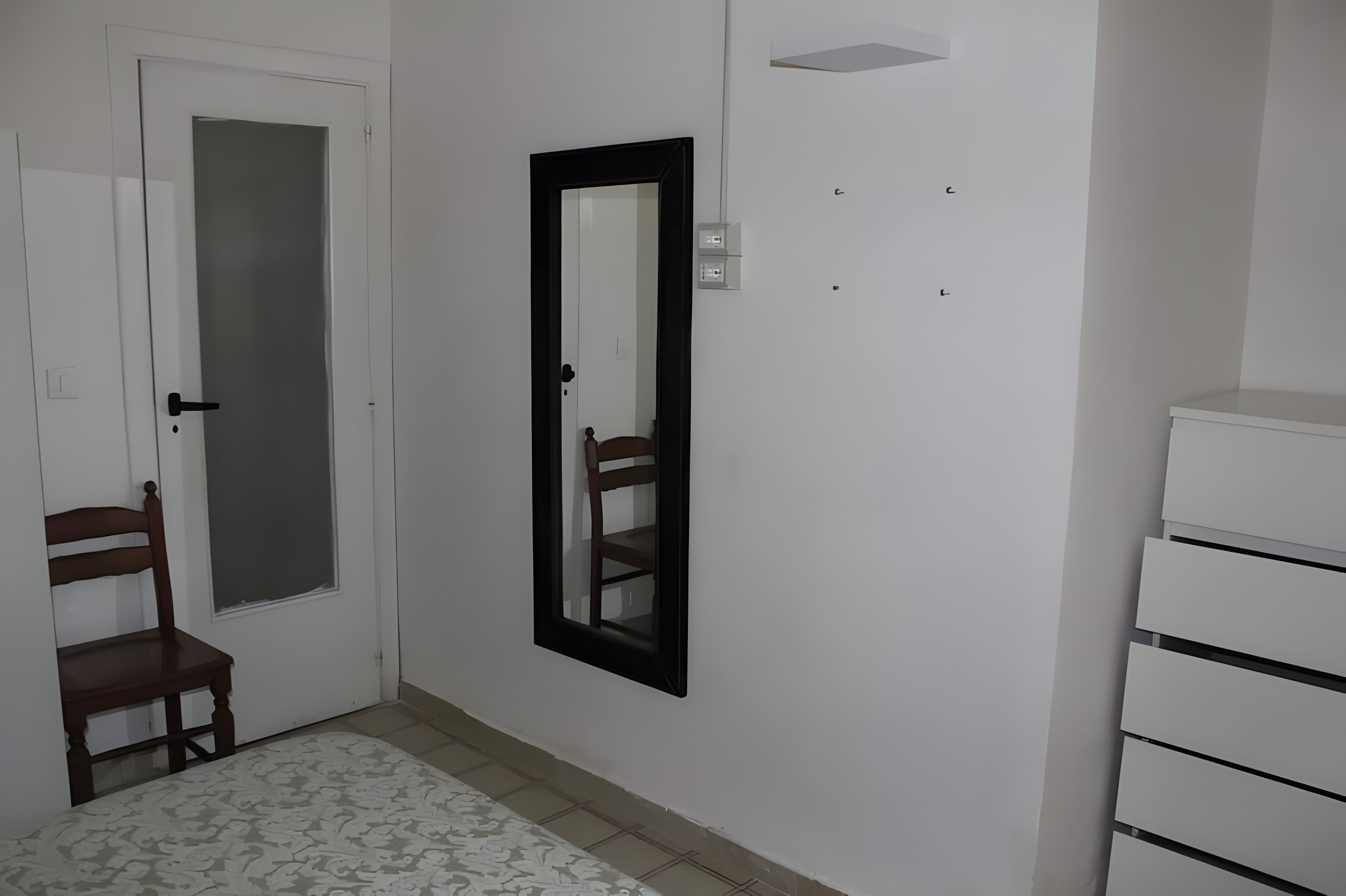 A hallway with a door, a mirror, a chair, and a white dresser.