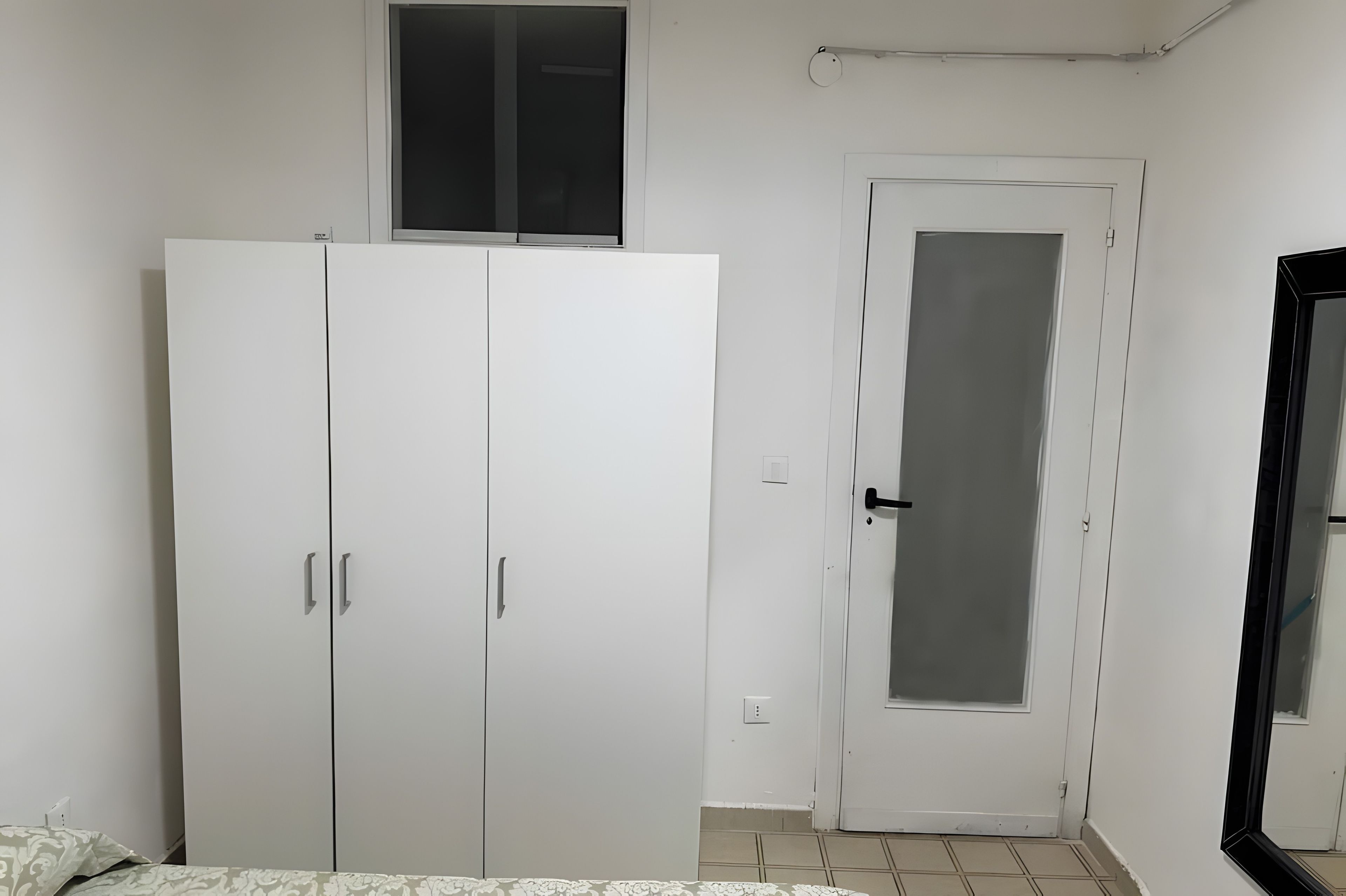 A room with a large wardrobe, a door with a frosted glass panel, and a window above the wardrobe.