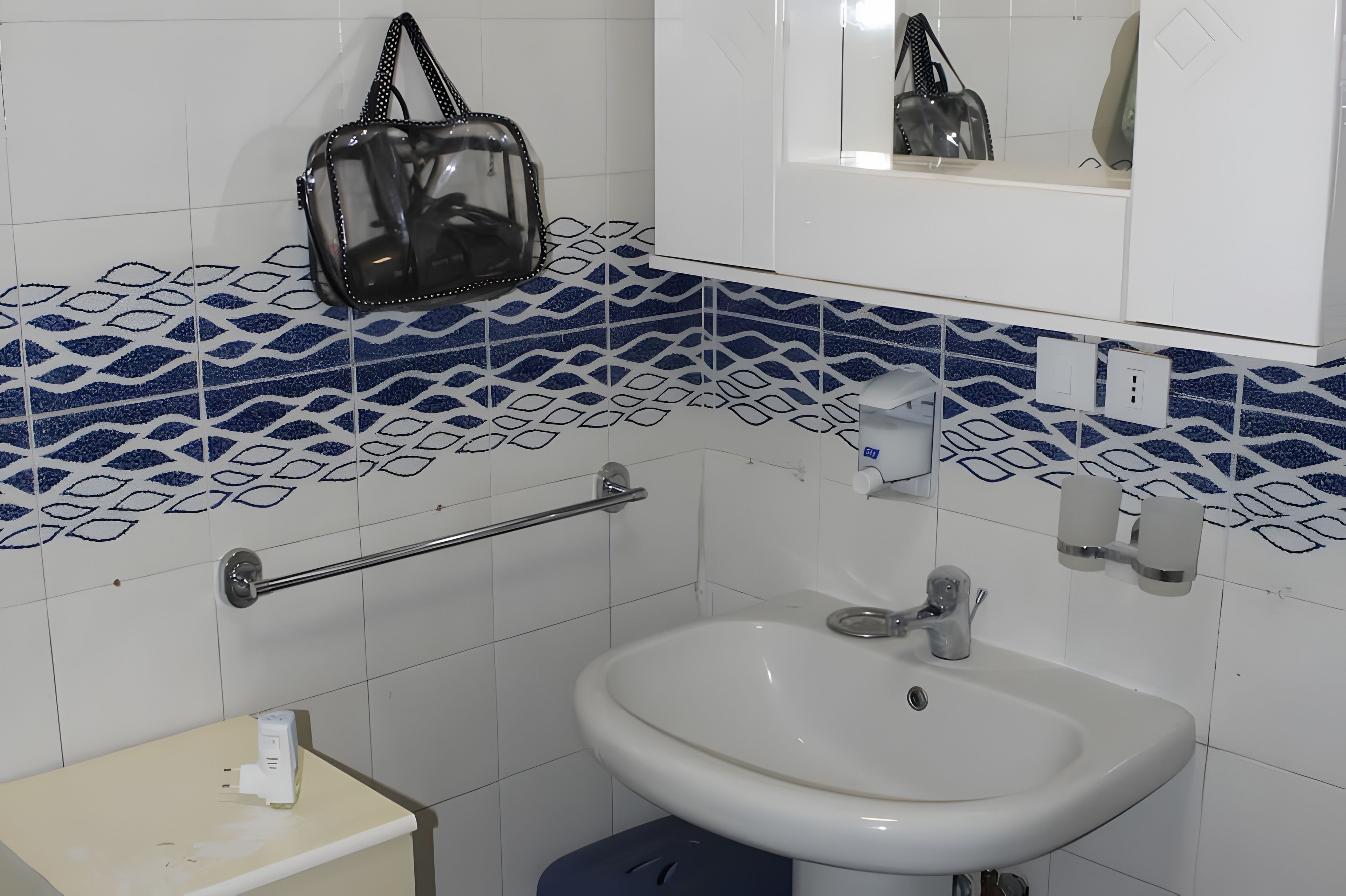 A bathroom with a white sink, a towel rack, a mirror, and a patterned tile backsplash.