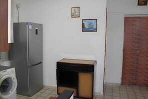 A compact kitchen with a refrigerator, washing machine, and a stove. There are two framed pictures on the wall.