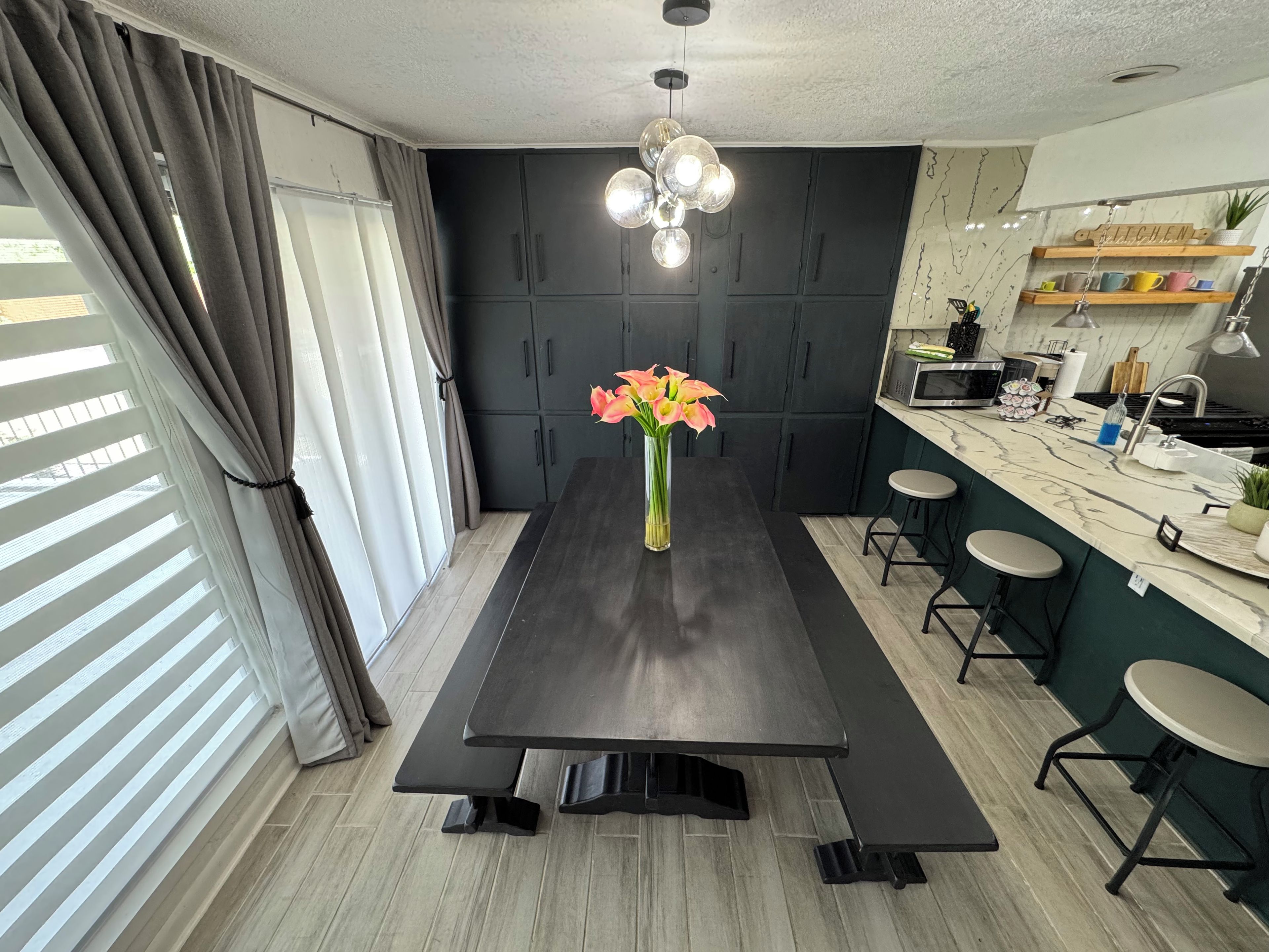 Una cocina moderna con armarios oscuros, encimera de mármol y comedor con mesa negra y bancos.