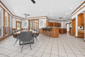 Een ruime keuken met een centraal eiland, houten kastjes en een eethoek met een grote tafel en stoelen.