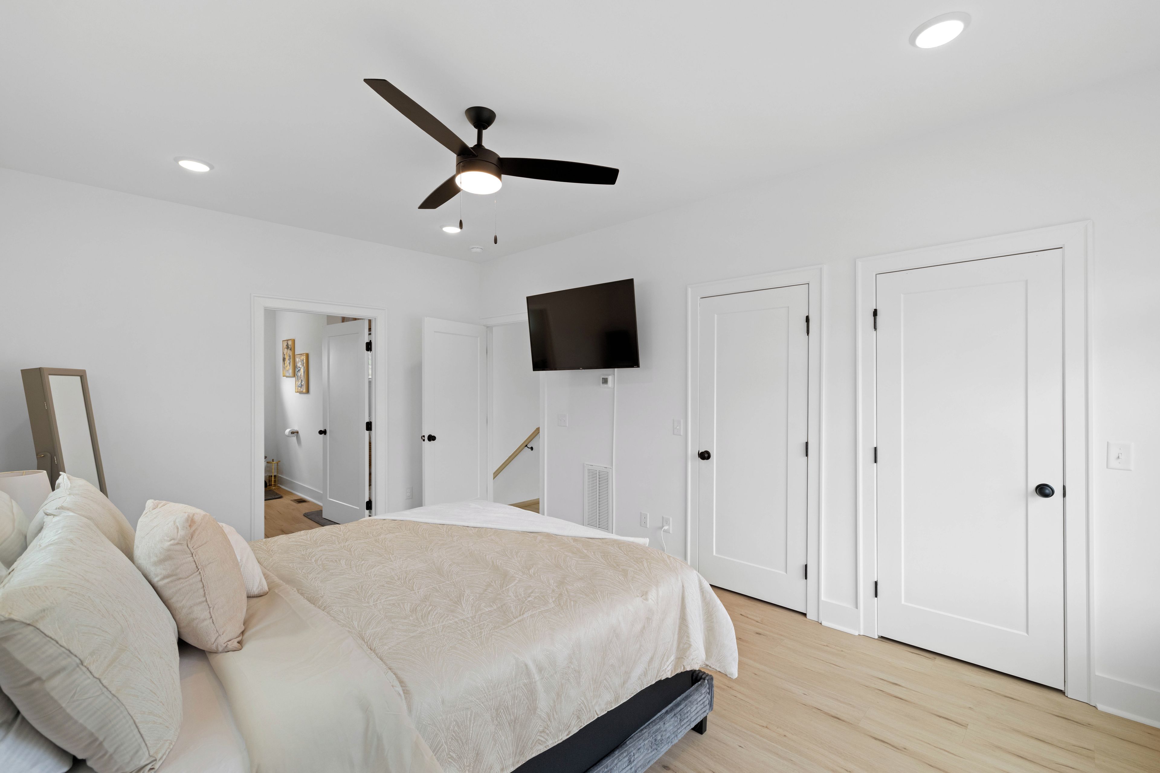 A bedroom with a bed, a ceiling fan, a TV, and white doors.