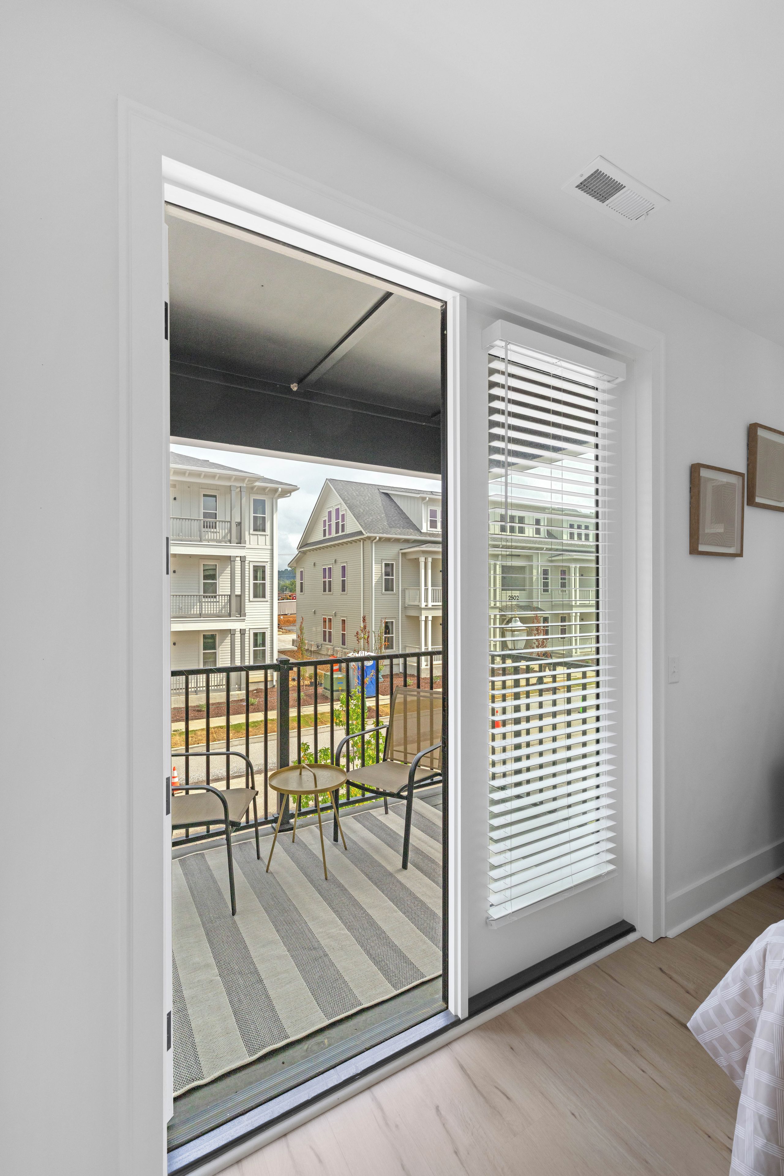 A room with a sliding glass door leading to a balcony with a metal railing and a small table.
