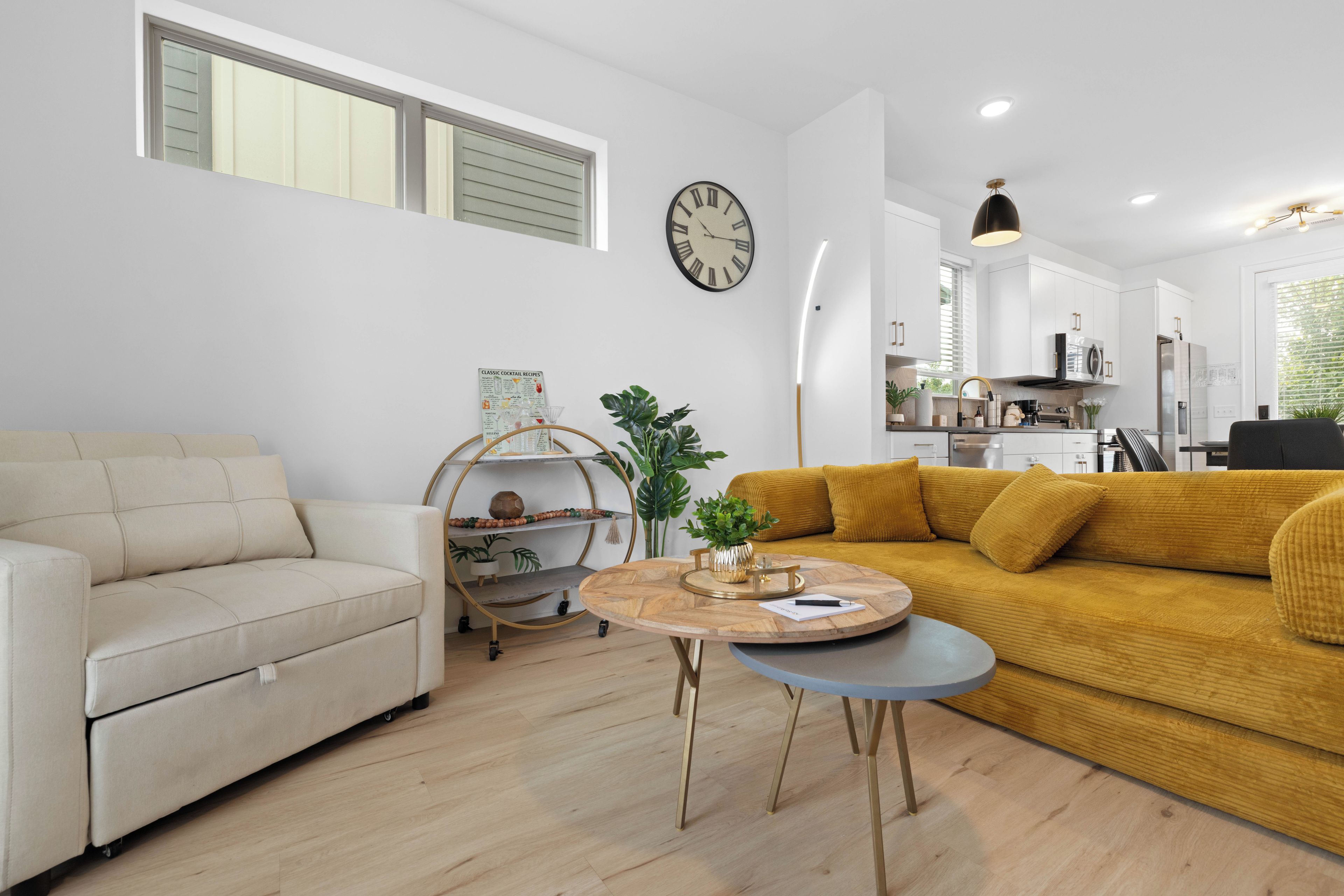 A modern living room with a sofa, a coffee table, a clock, and a kitchen in the background.
