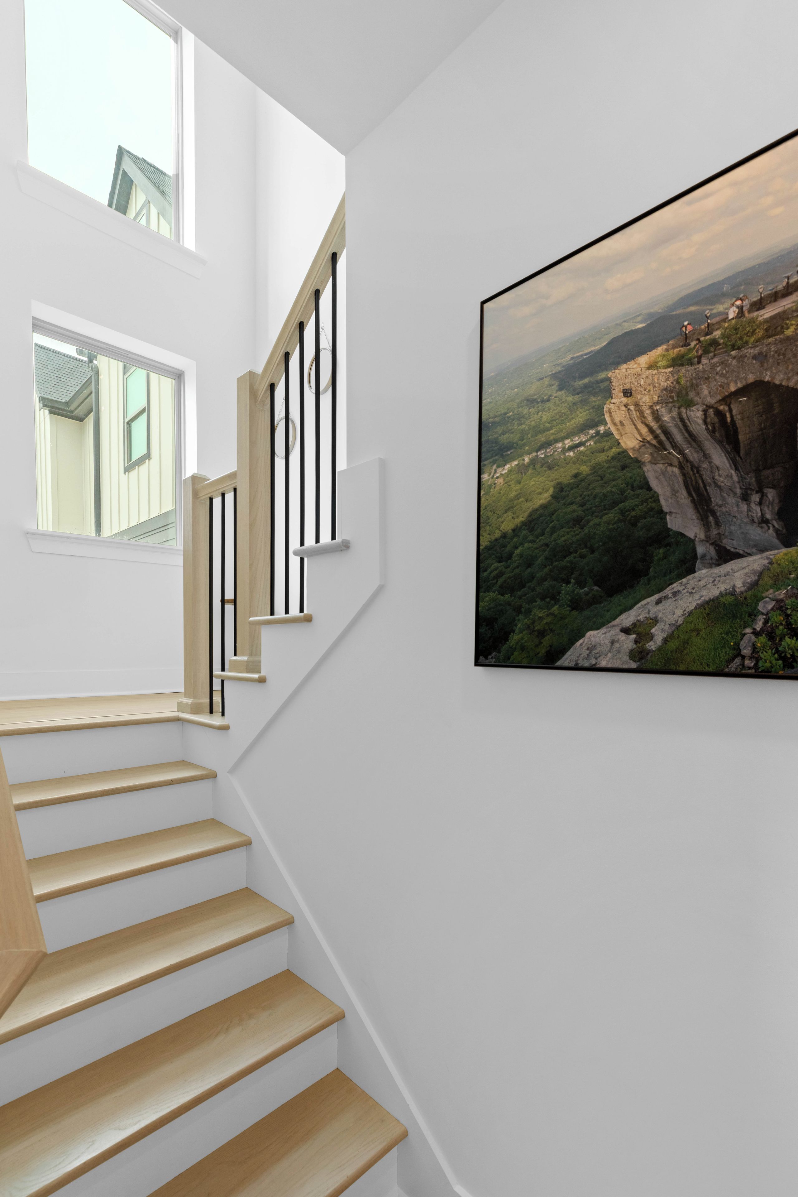 A staircase with wooden steps and black railings, leading to a landing with a large framed photograph of a mountainous landscape.
