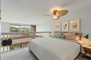 Ein Schlafzimmer mit einem Bett, einem Deckenventilator, Wandkunst und einem Balkon mit Blick.