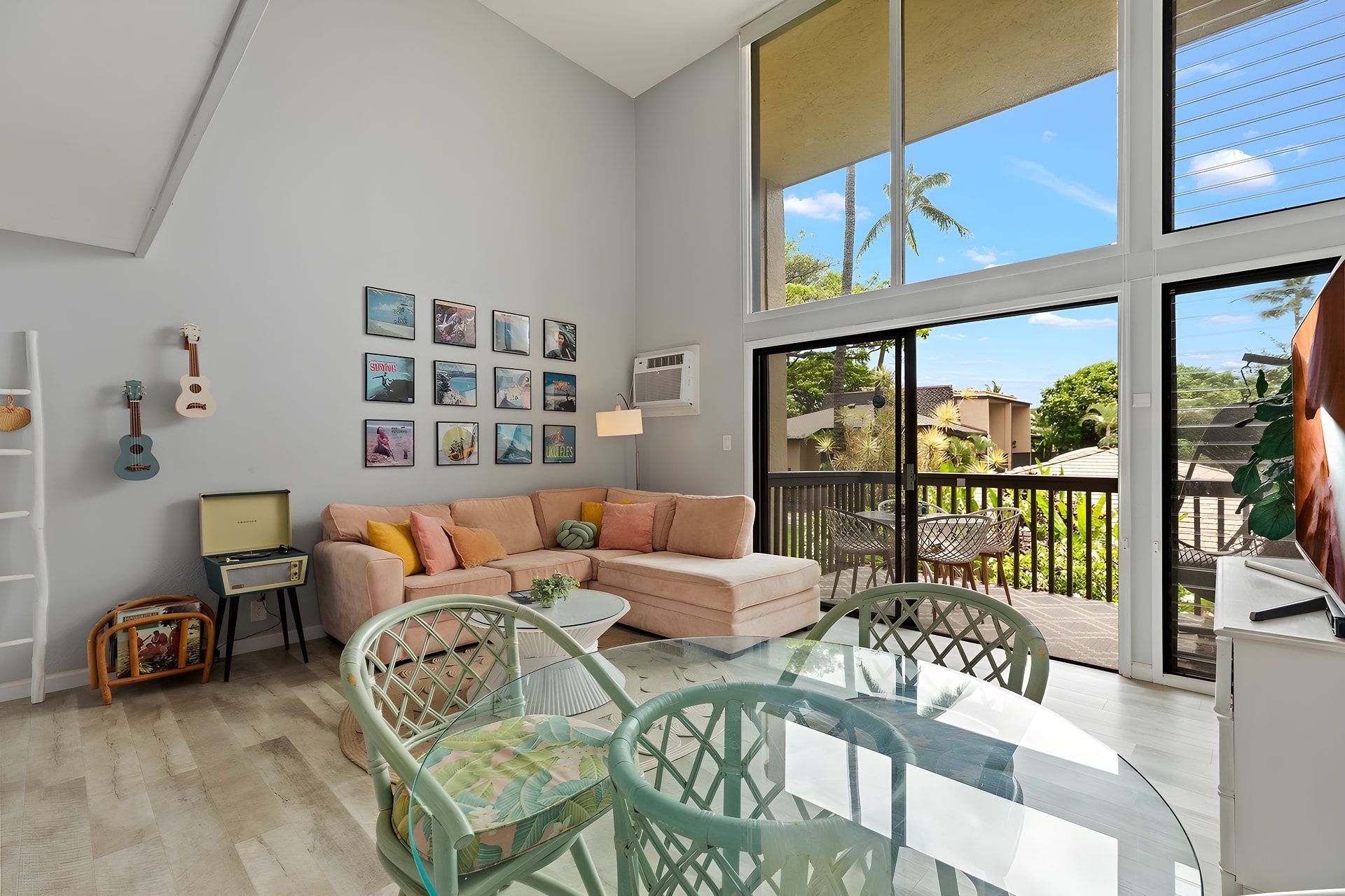 A spacious living area with a large window, a sofa, a glass coffee table, and a dining table with chairs.
