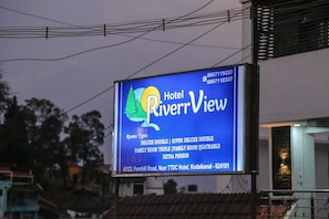 Un cartel de hotel con el nombre 'Hotel RiverrView' y una lista de tipos de habitaciones, incluyendo Habitación Doble Deluxe, Habitación Doble Super Deluxe, Habitación Familiar Triple, Habitación Familiar Cuádruple y Persona Adicional.