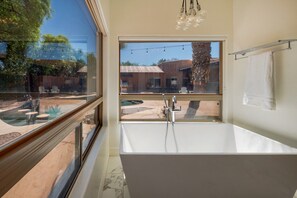 Ein modernes Badezimmer mit einem großen Fenster, einer Badewanne und Blick auf einen Außenpool.