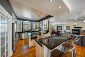 A modern kitchen with a central island, stainless steel appliances, and a dining area with red chairs. - House & Guesthouse / Pool & Hot Tub / 5 BR 5 BA (Tucson)