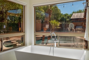 A bathroom with a white bathtub, a window, and a view of the outdoors. - House & Guesthouse / Pool & Hot Tub / 5 BR 5 BA (Tucson)