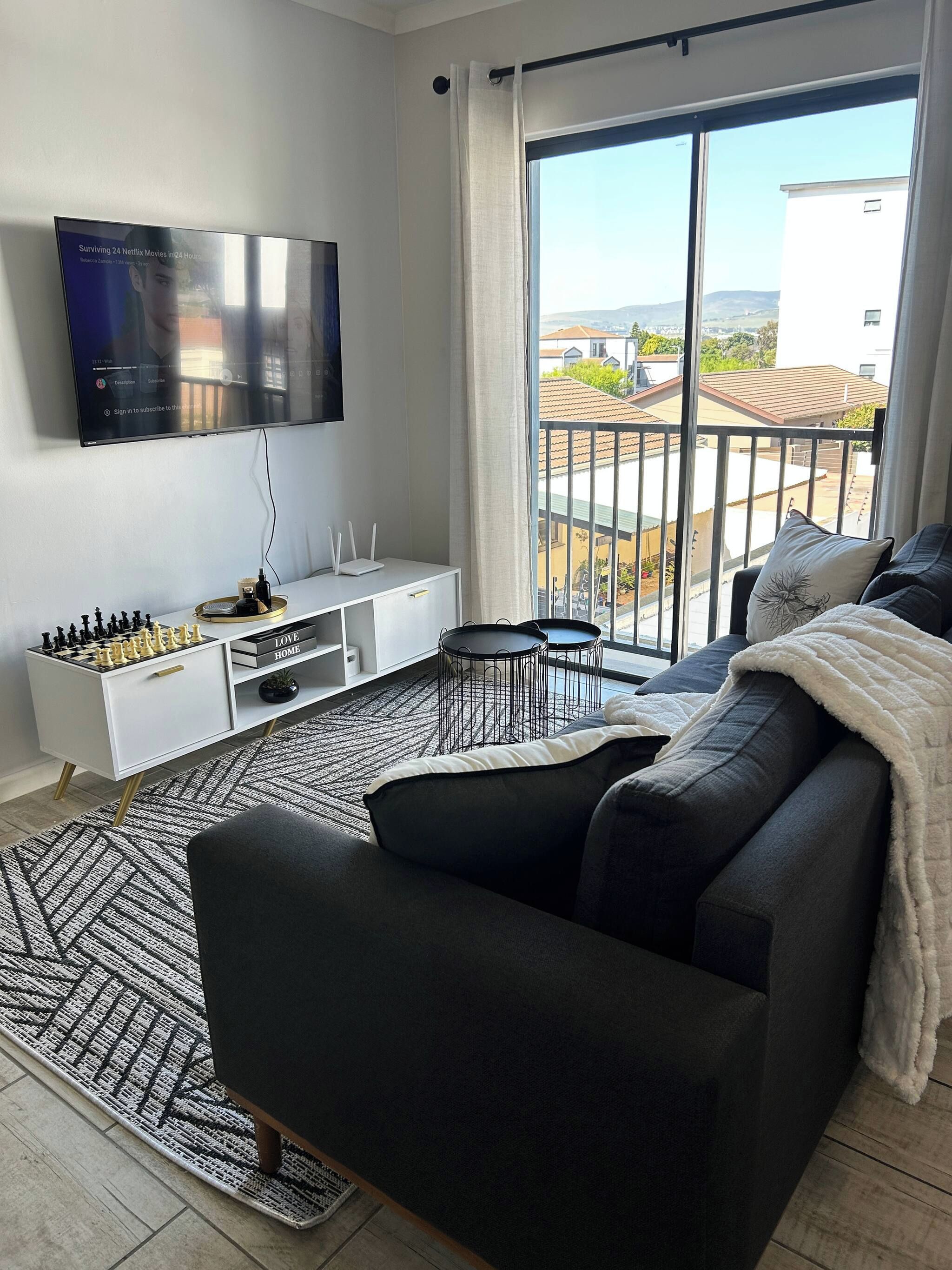 A modern living room with a flat-screen TV, a sofa, a coffee table, and a view of the outside.