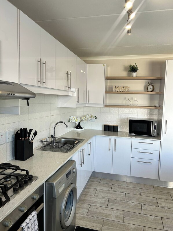 Una cocina moderna con gabinetes blancos, electrodomésticos de acero inoxidable, horno empotrado y microondas.
