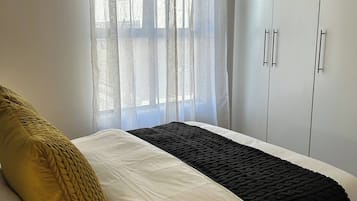 A bedroom with a bed, a wardrobe, and a window with curtains.