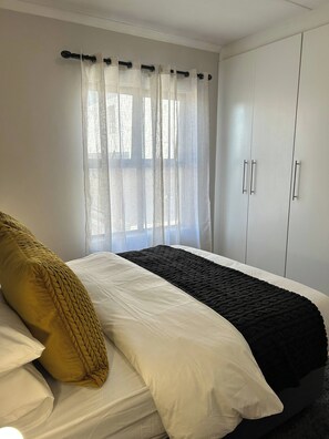 A bedroom with a bed, a wardrobe, and a window with curtains. - Relax, Unwind & Feel at Home (Cape Town)